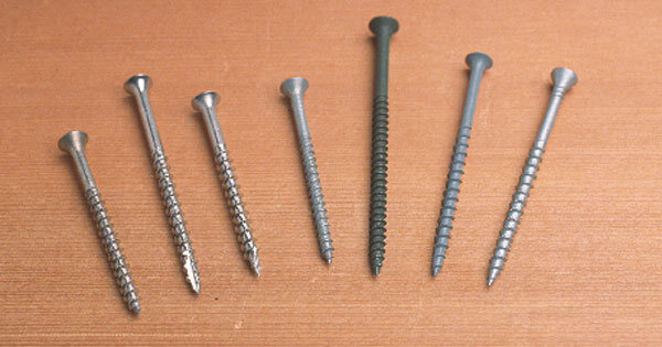 Seven various sized metal nails and screws arranged in ascending order on a wooden surface.