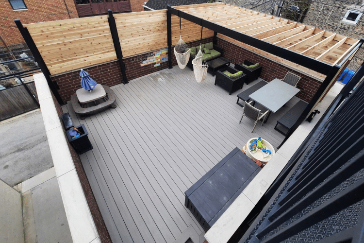 Overhead view of a modern rooftop deck with gray flooring, contemporary furniture, and a wooden privacy wall.