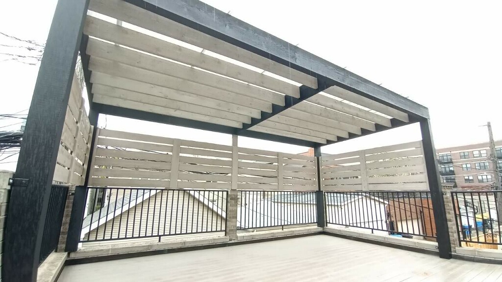 Open wooden pergola with horizontal slats on a rooftop deck, overlooking urban surroundings.