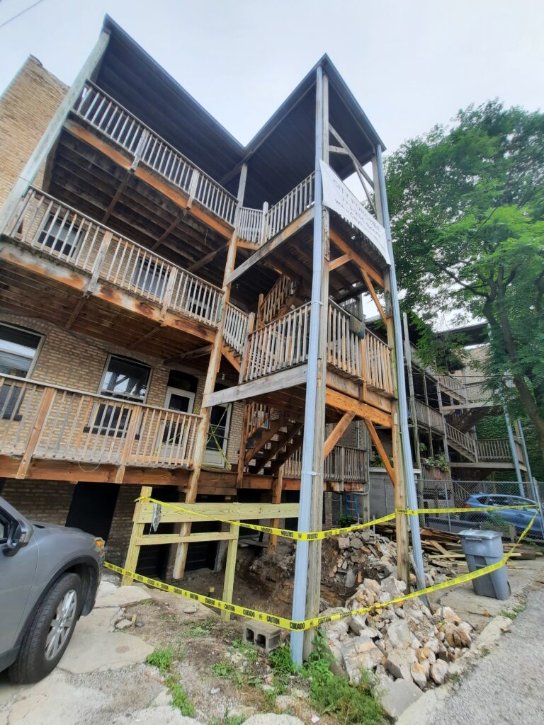 Three-story wooden porch under repair, secured with caution tape, on a brick building. (Home owners association)