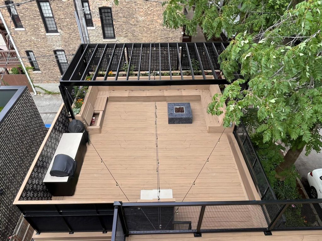 Overhead view of a rooftop deck with beige flooring, black railing, surrounded by trees and buildings