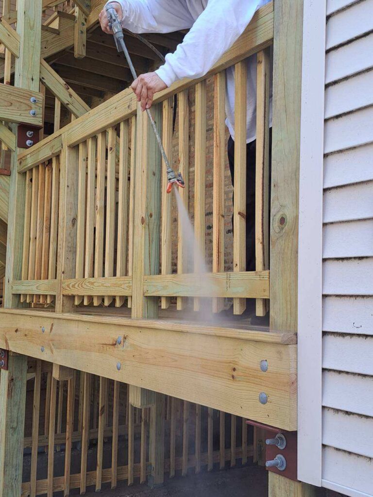 Person pressure washing a new wooden gate, showing water spray and wood details