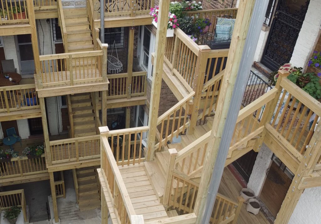 An overhead view of a wooden fire escape with multiple staircases connecting various levels of an apartment complex. ( city Porches )