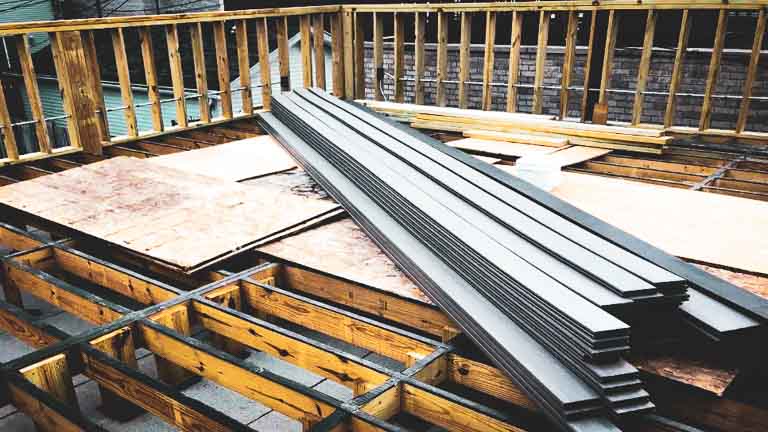 A stack of dark composite decking boards laid on a wooden framework at a construction site.