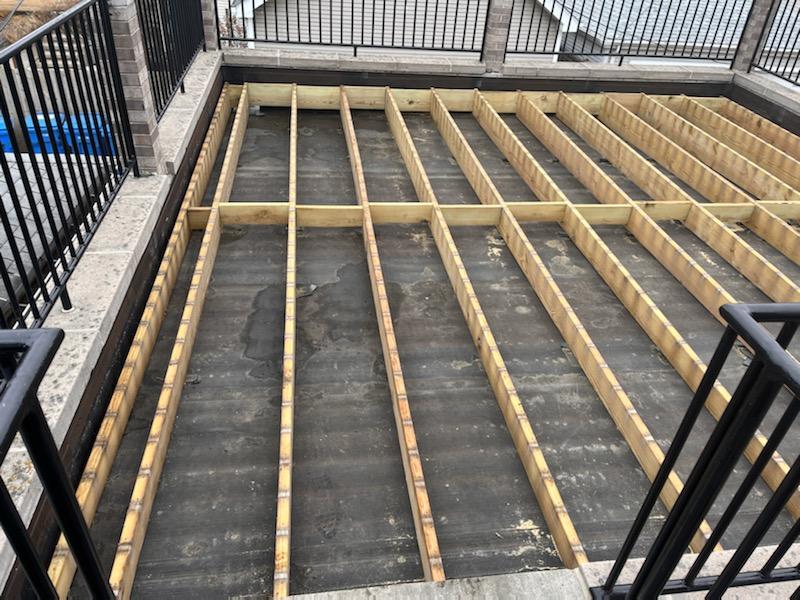 Aerial view of a wooden deck under construction with a black ledger railing on the sides.