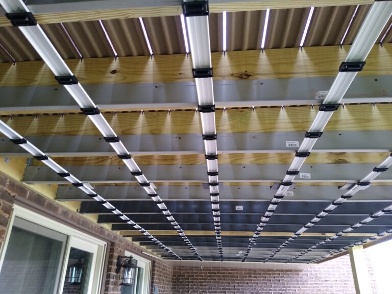 Underside of a metal roof structure with wooden beams and black steel supports, viewed from within a covered patio area.-Roof Joist