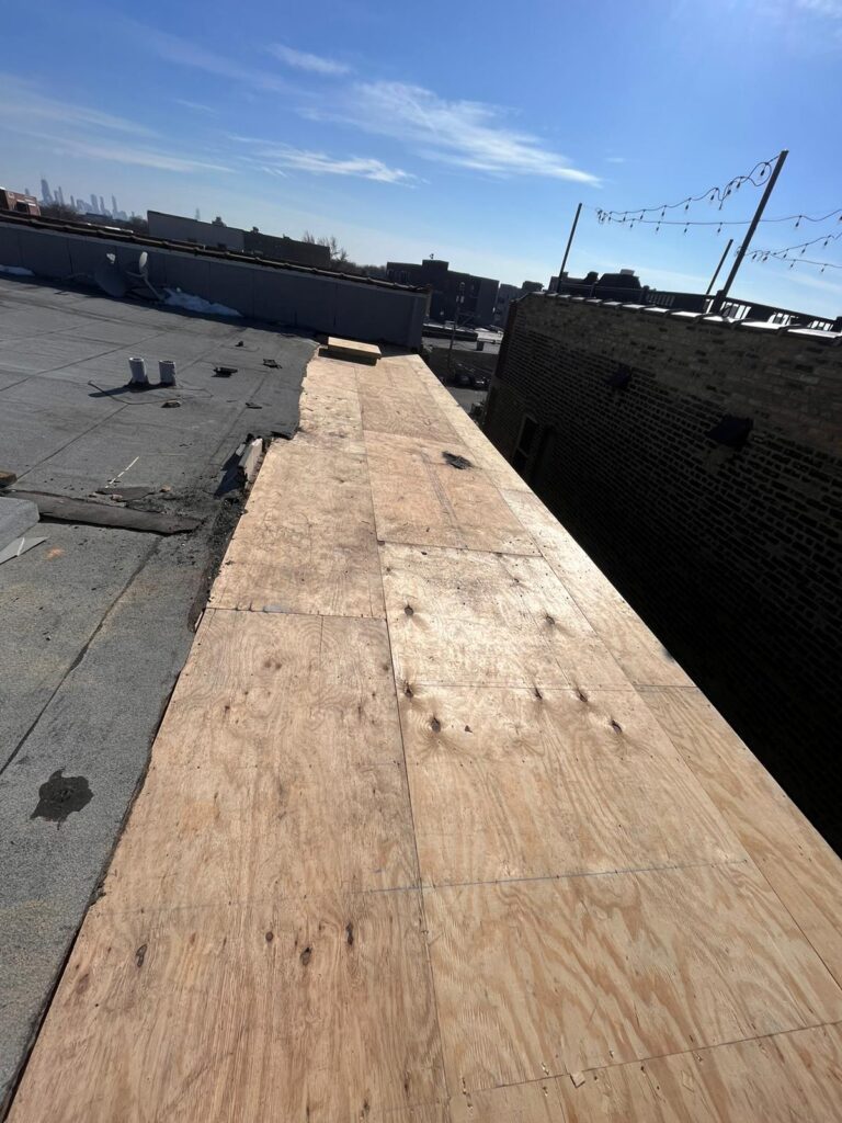 Deck sheathing in progress on a rooftop with plywood boards laid out, under a clear blue sky