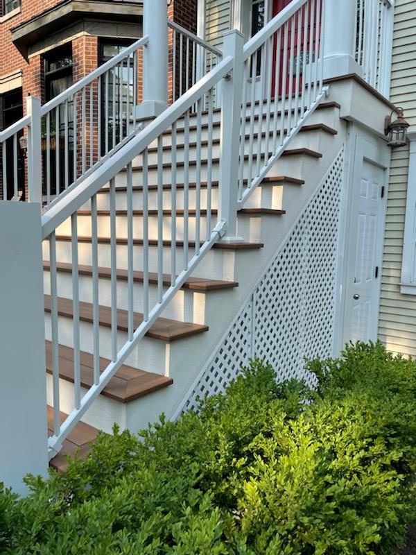 White stairway with wooden steps and lattice side panel beside green shrubbery.-Easy Porch Steps