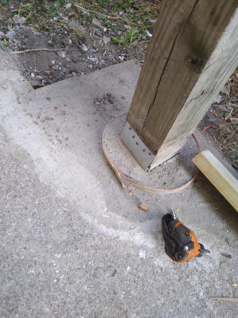 Concrete base with a wooden post secured by a metal bracket next to a tape measure on the ground.