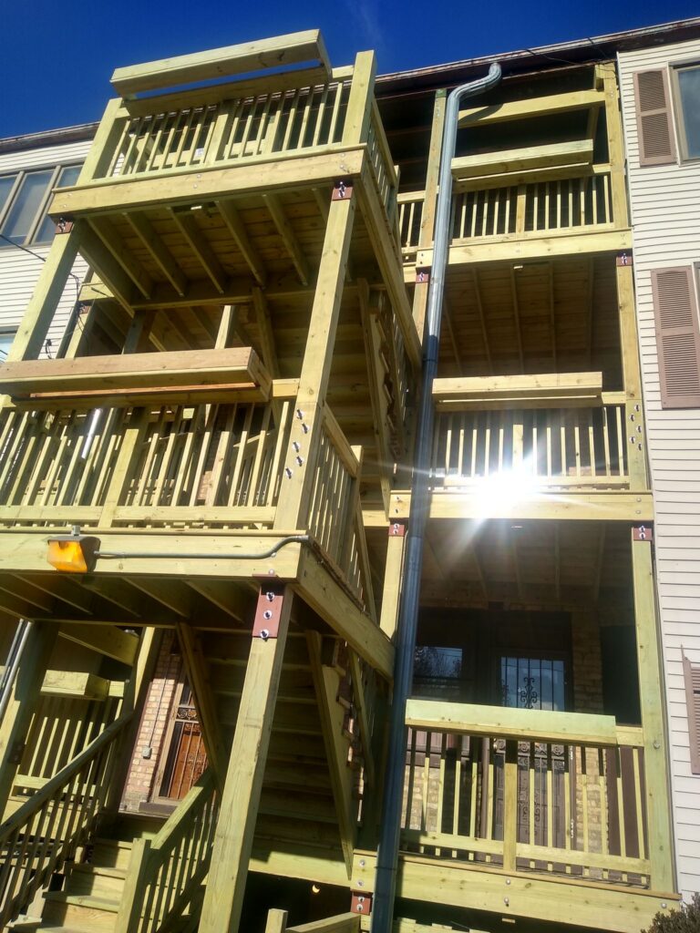 Multi-level porch wooden deck with stairs,railings and column on a bright day, attached to a house.
