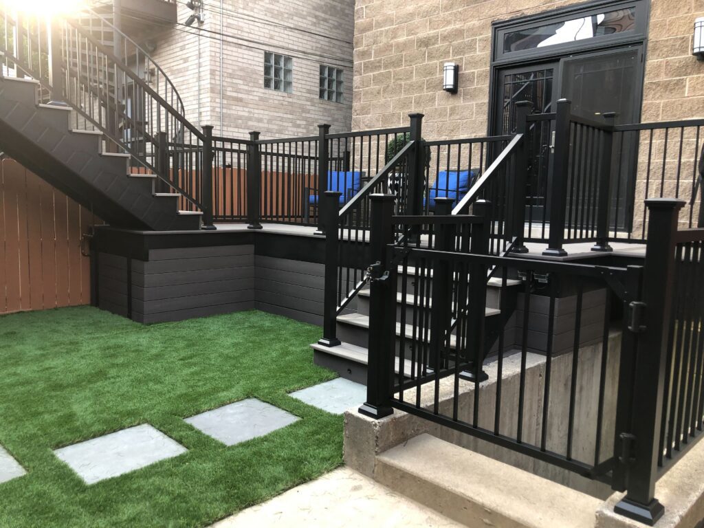 A multi-level deck with artificial turf and stepping stones, flanked by a black metal staircase and matching railing.