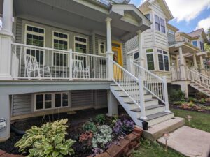 Charming home with a white porch and railing, accented by a yellow door, with surrounding lush garden and a stone path- Front Porch Ideas
