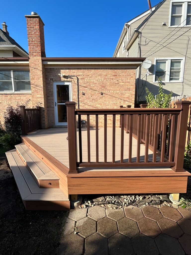 Backyard wooden deck with built-in steps and brown railing kits, adjacent to a brick house under a clear blue sky.-Low Railing