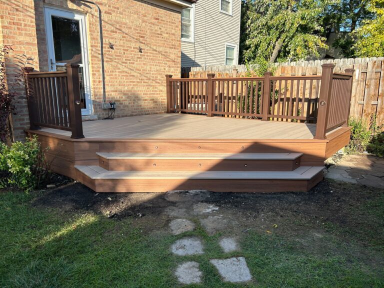 Spacious wooden deck with steps and railings adjoining a brick house, set against a backdrop of a fenced yard and greenery.-Deck Replacement - Building Deck Stairs