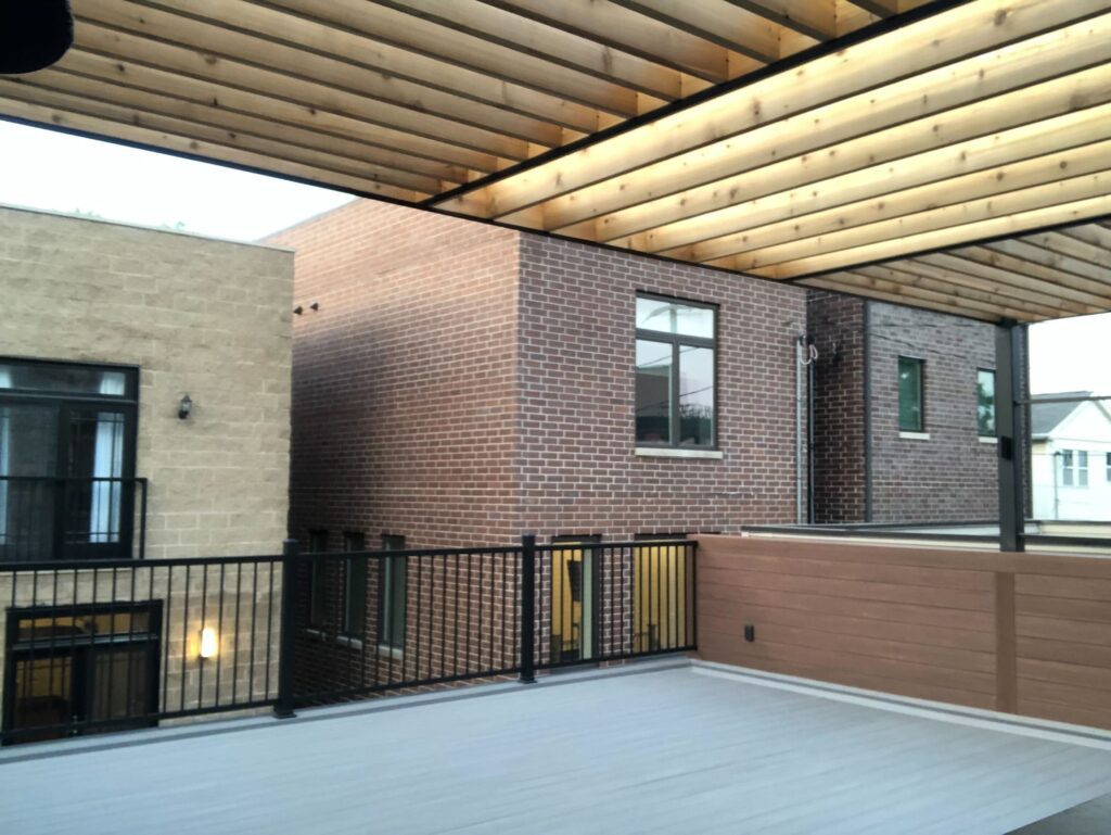 Rooftop deck with wood floors, pergola, and modern black railing kits beside a brick building.-Roof Washing
