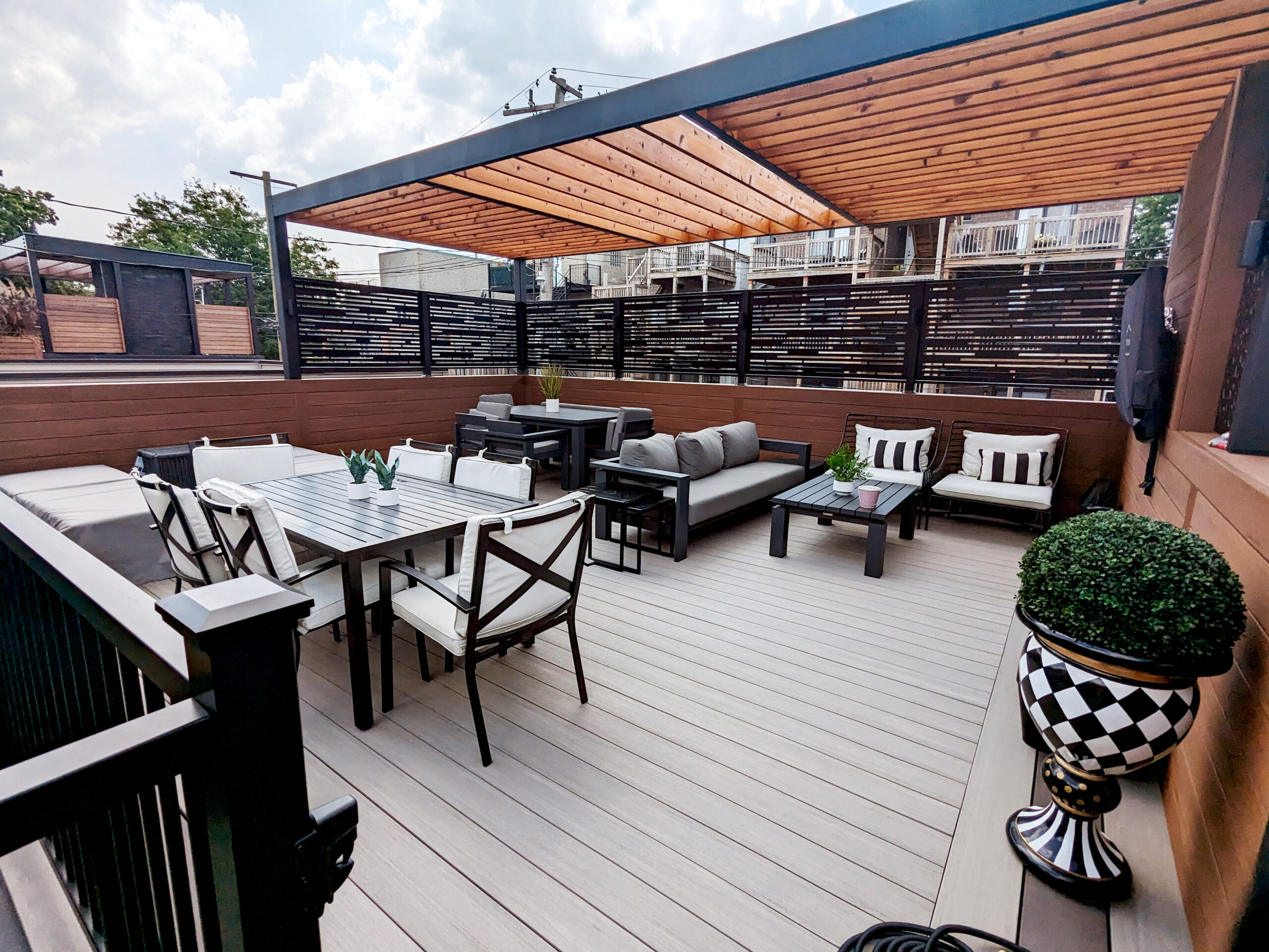 Modern outdoor deck with dining table, comfortable seating, wooden slatted privacy screens, and decorative planters.