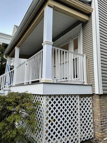 Elevated porch with white railings, lattice skirting, and a covered ceiling on a classic home.