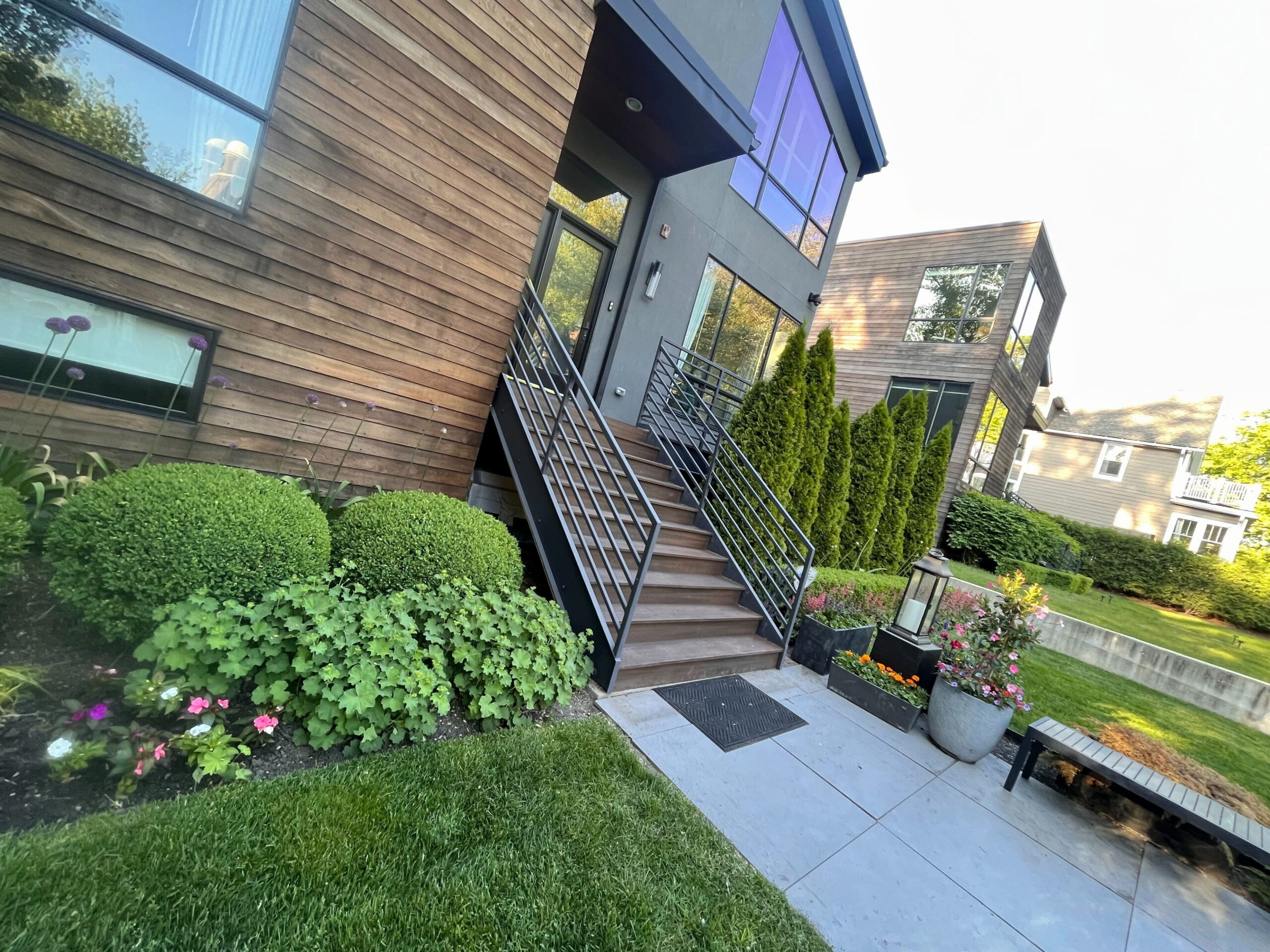 Modern house with wood and stucco exterior, black railings, landscaped yard, and stylish front stairs.








