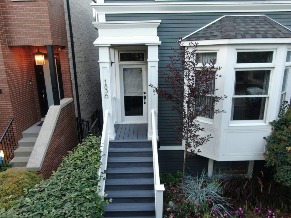 A stylish front porch with a dark blue exterior, white trim, and a glass-paneled door. The wooden staircase with white railings leads to an inviting entrance framed by decorative columns. A landscaped garden with flowers and shrubs adds warmth to the home’s curb appeal.







