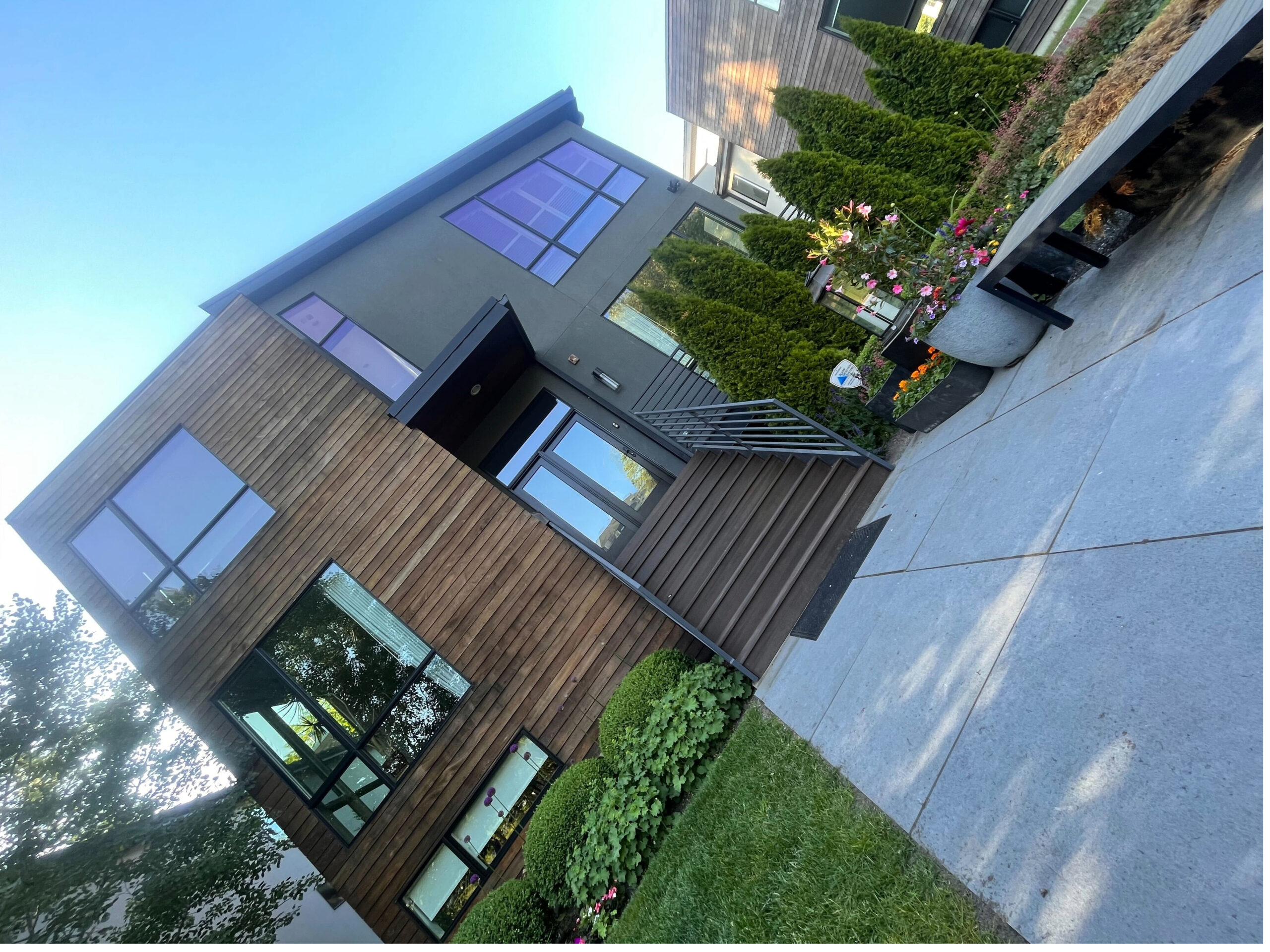 Modern house with wood and stucco exterior, large windows, and landscaped front yard with flowers.