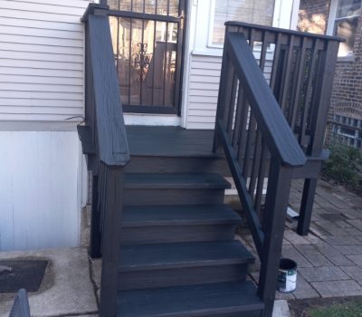 Freshly painted dark grey wooden stairs with white trim leading to a house entrance.